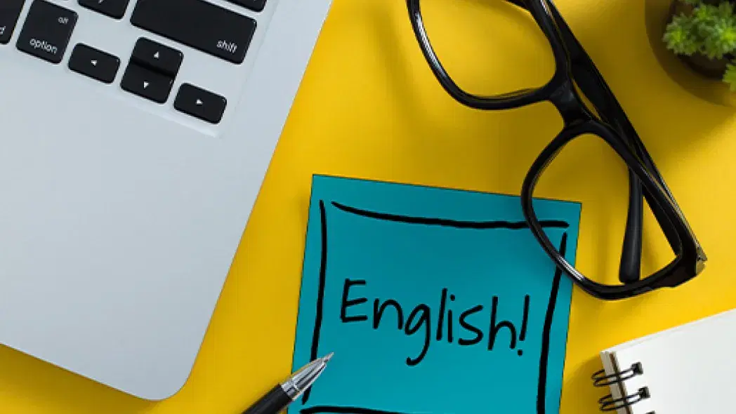 Englishと書かれた紙とパソコンとペンとメガネが映った写真