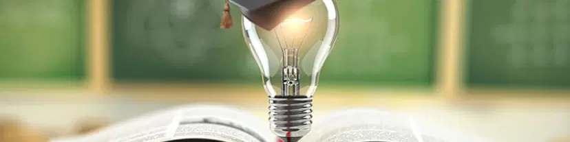 本の上に置かれた点灯する電球と学士帽